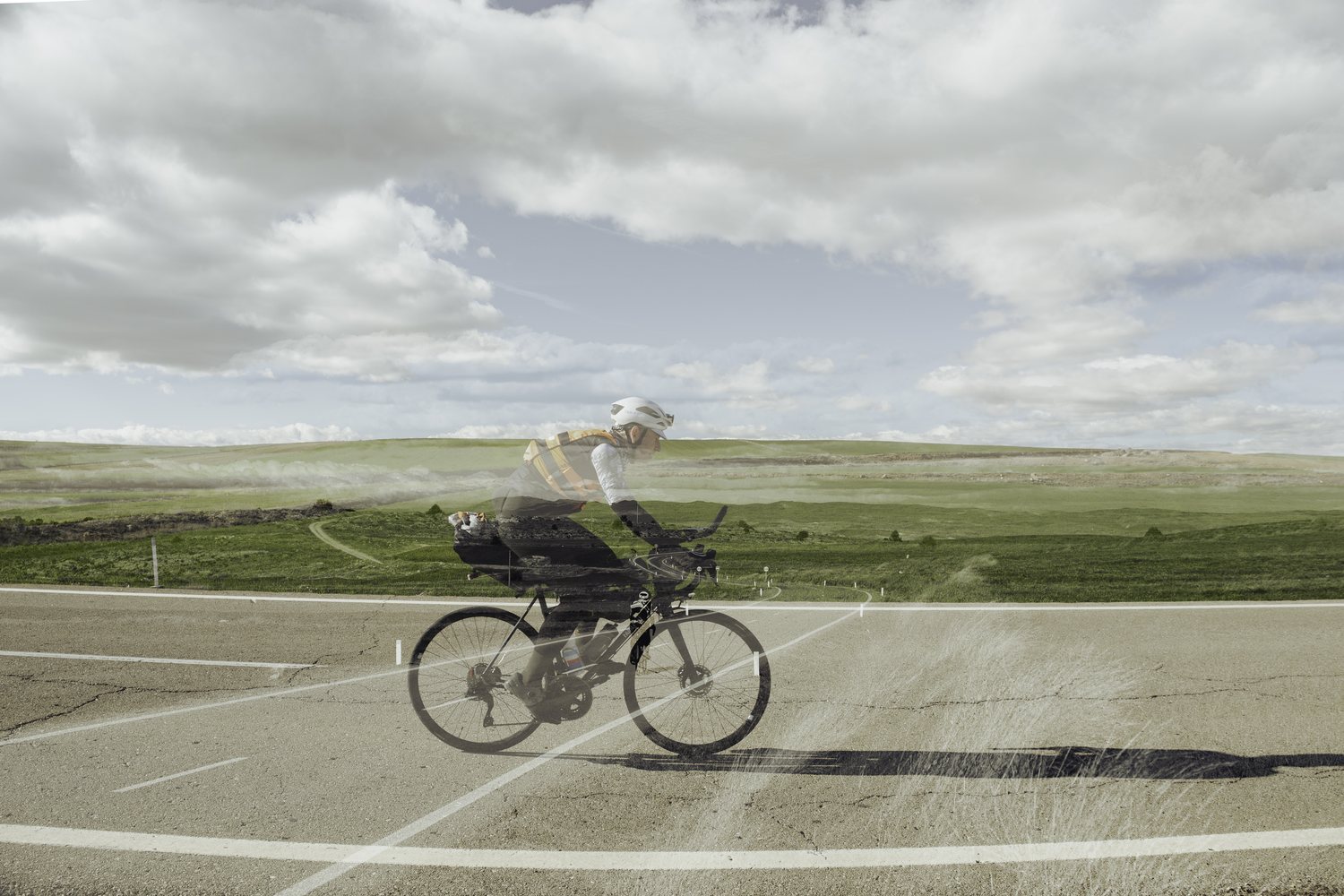 Double exposure of a rider on a loaded bike crossing a wide green plateau under big clouds, TURN04 in Spain